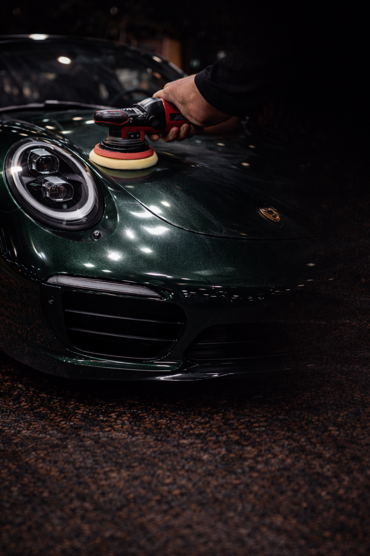 Gezielte Lackaufbereitung am Porsche Gezielte Auto Lackaufbereitung und Defektkorrektur mit der Poliermaschine auf dem dunkelgrünen Lack eines Porsche.