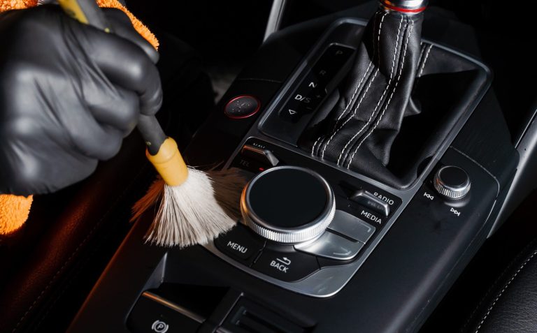 Detailaufnahme einer schonenden Pinselreinigung an der Mittelkonsole und Leder-Armlehne – Fokus auf Smarte Fahrzeugpflege im Innenraum.